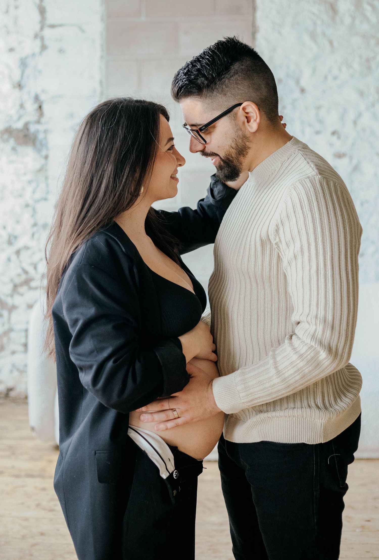 Loving couple embracing and cradling pregnant belly during indoor maternity photoshoot.