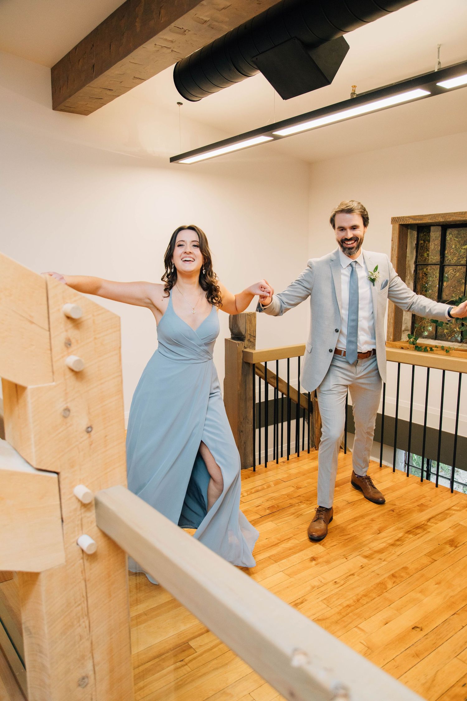 Smiling bridesmaid in blue dress and groomsman in gray suit making grand entrance at wedding.