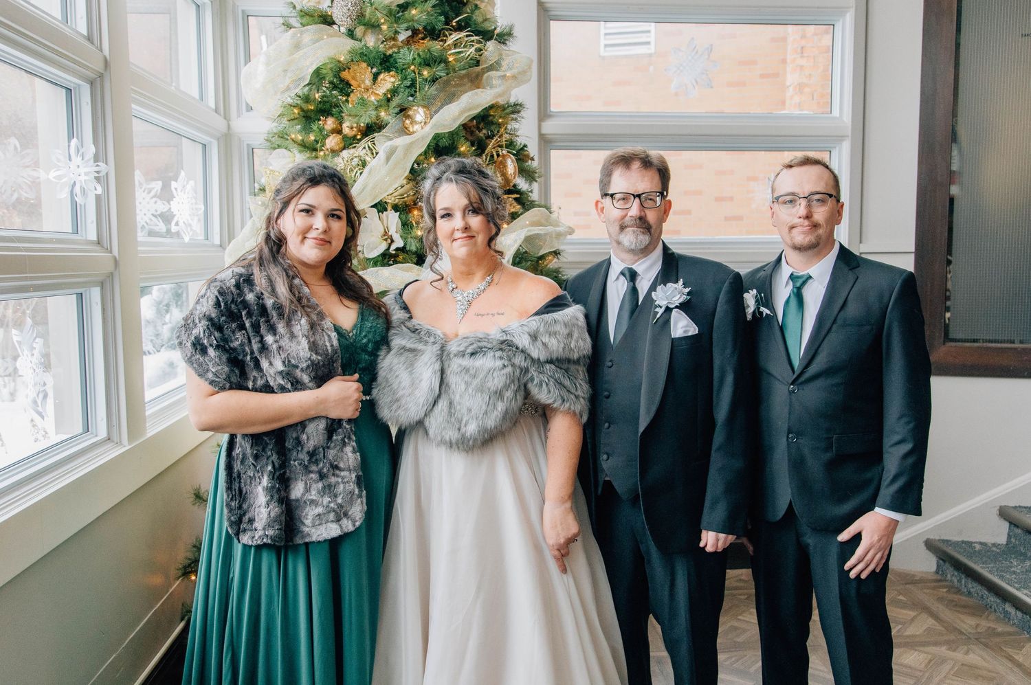 Bride, groom, and family members pose together beside a decorated Christmas tree indoors.