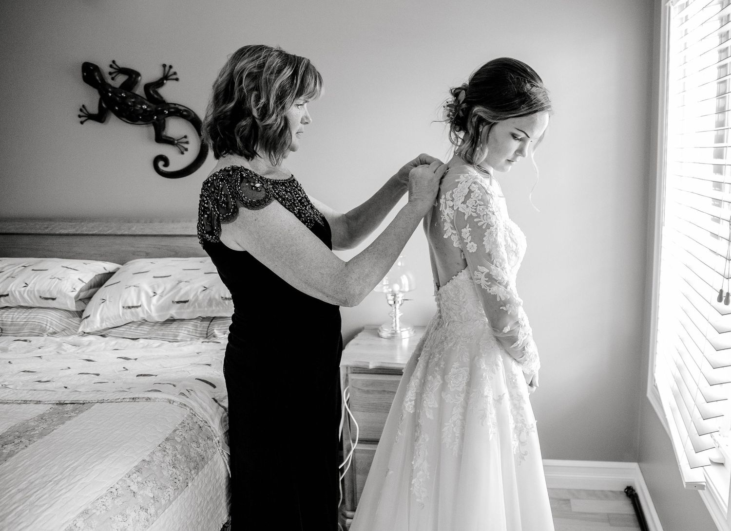 Black and white photo of mother helping bride button her lace wedding dress before the ceremony.