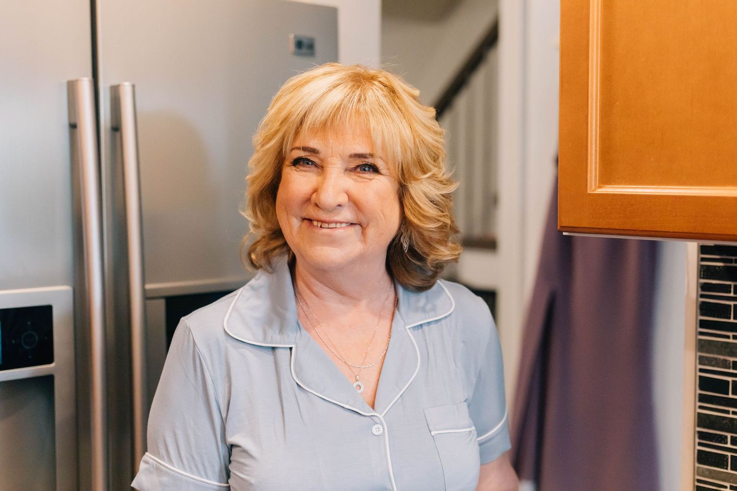 Smiling older woman in grey pajamas standing in modern kitchen during wedding preparations.