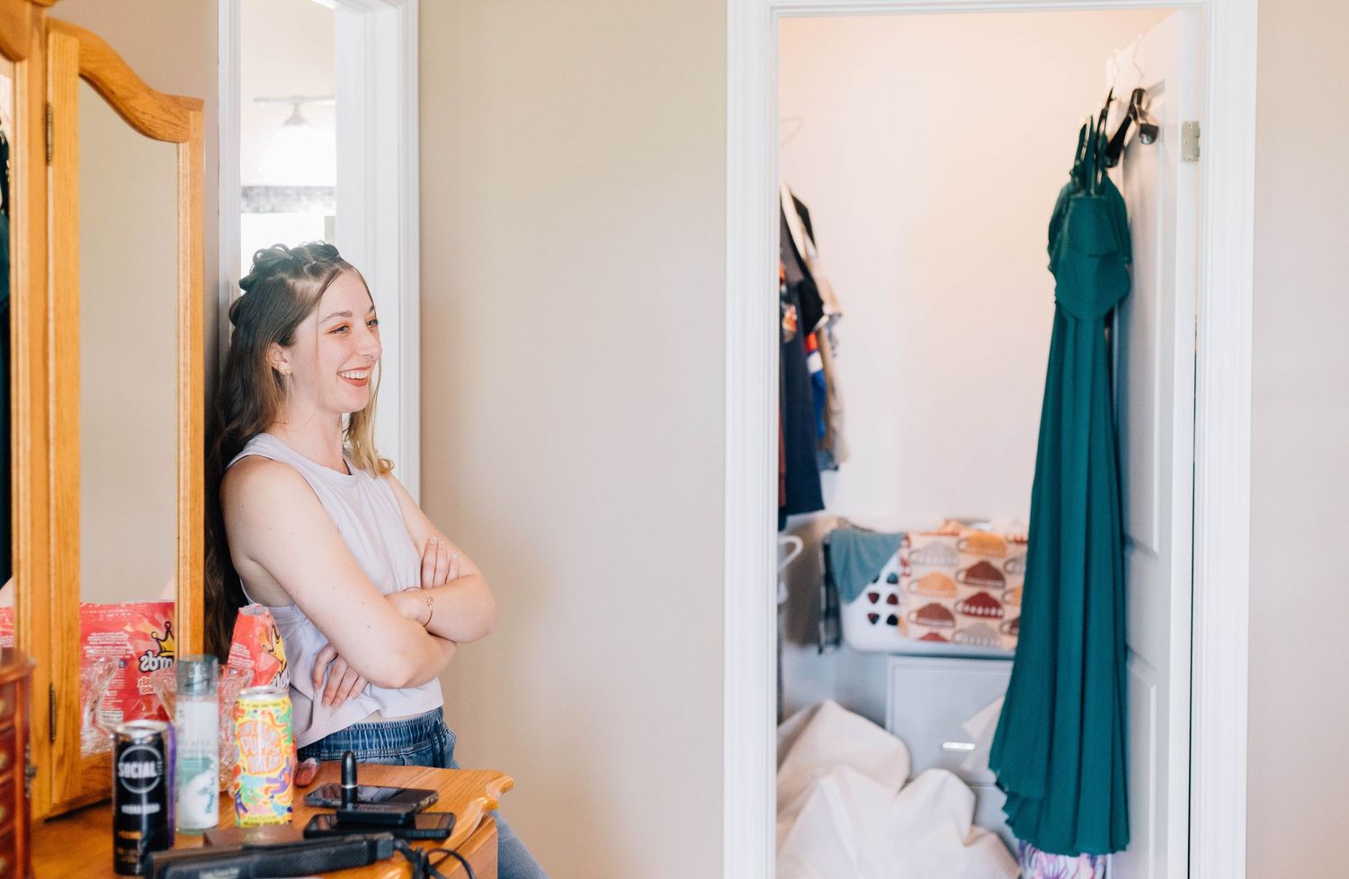 Smiling woman standing in doorway of closet with teal bridesmaid dress hanging inside.