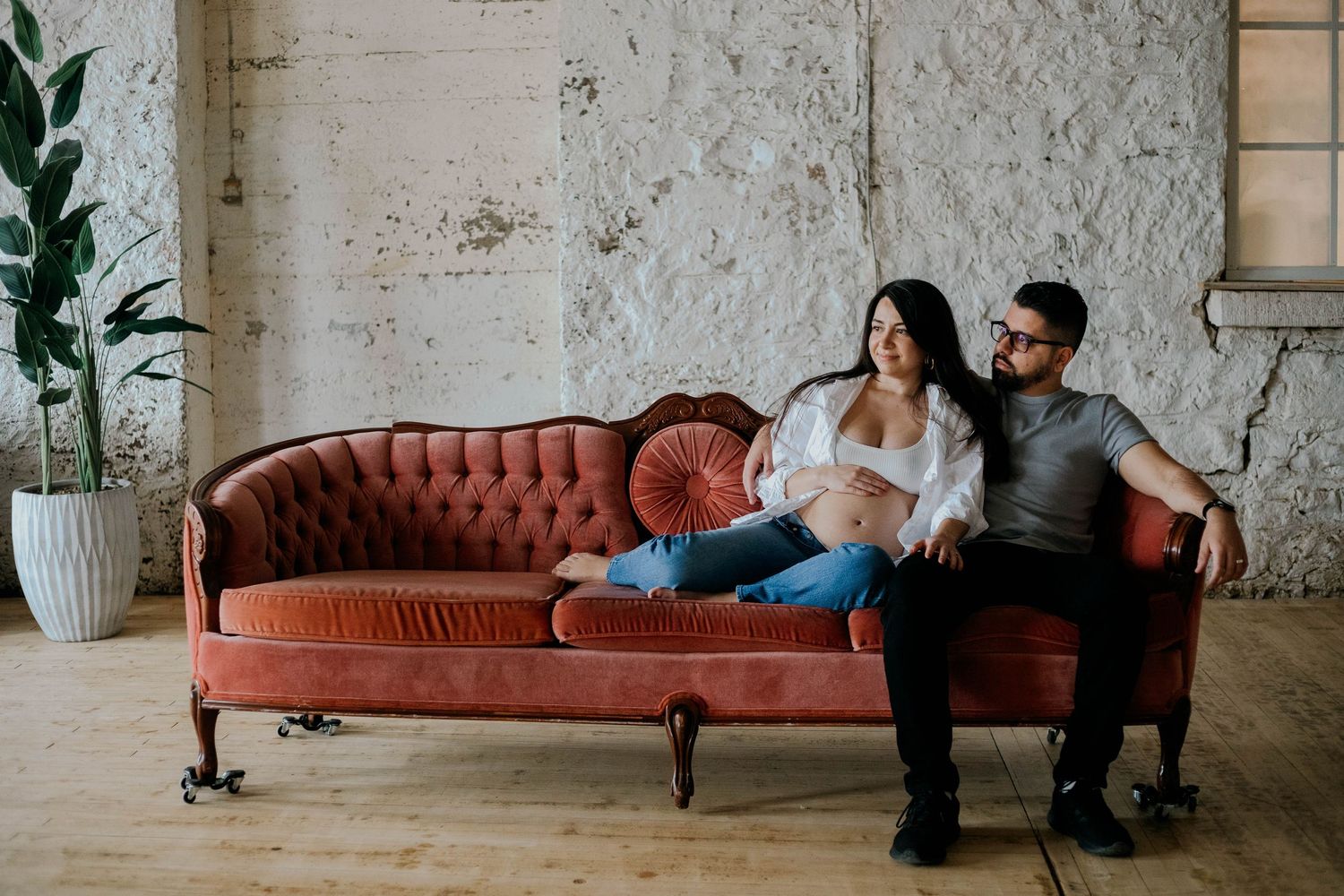 Expecting couple relaxing together on vintage velvet sofa during maternity photo session.
