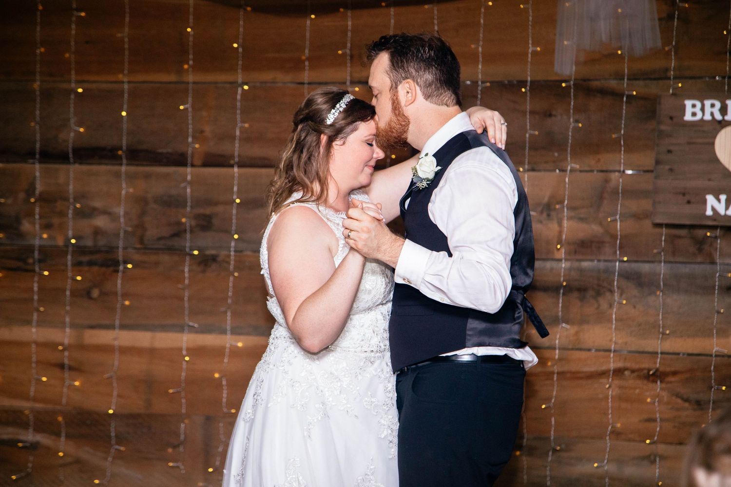 Bride and groom sharing an intimate first dance moment at rustic barn wedding with fairy lights.