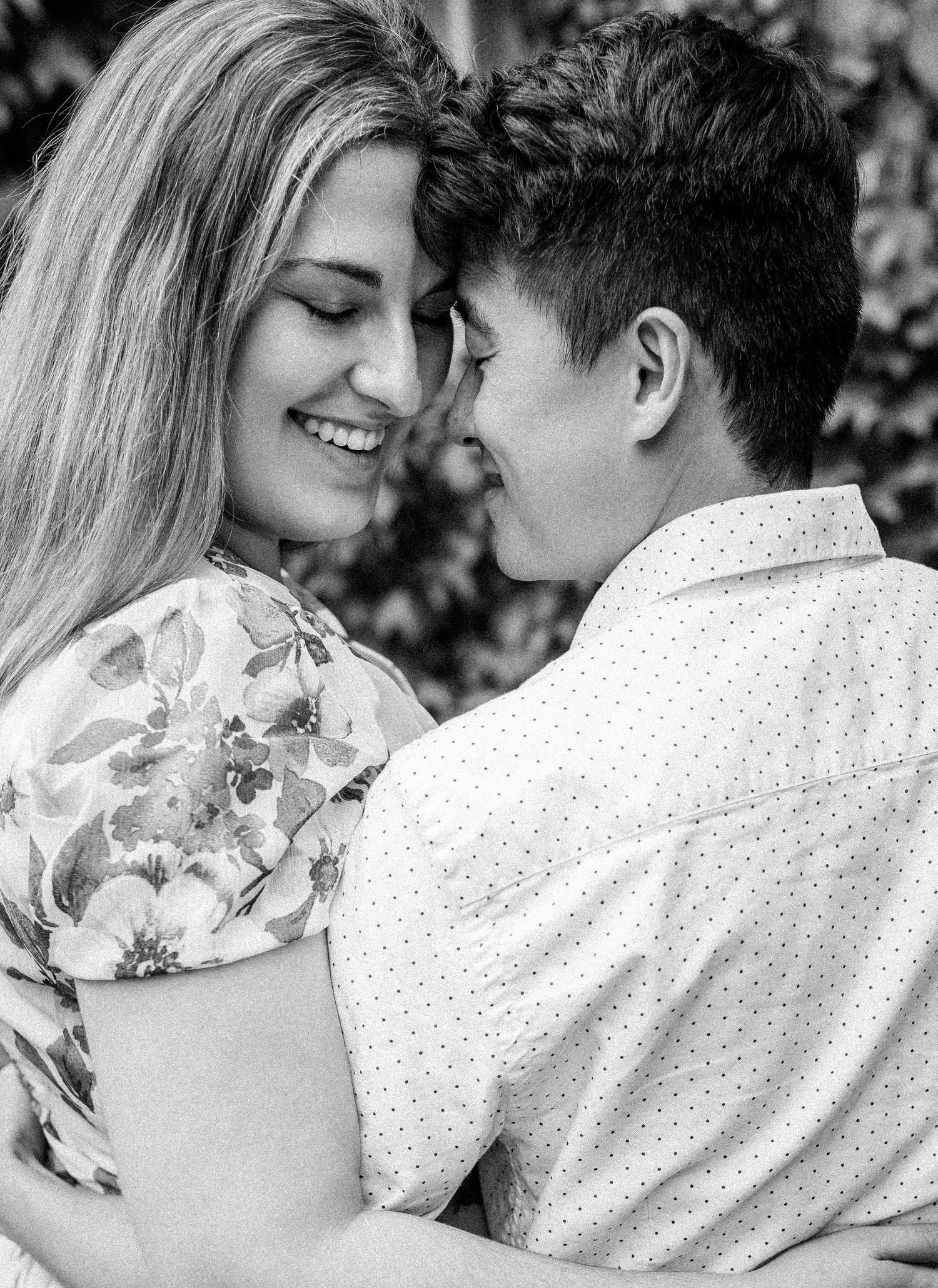 Black and white close-up of smiling couple touching foreheads in a tender romantic moment.