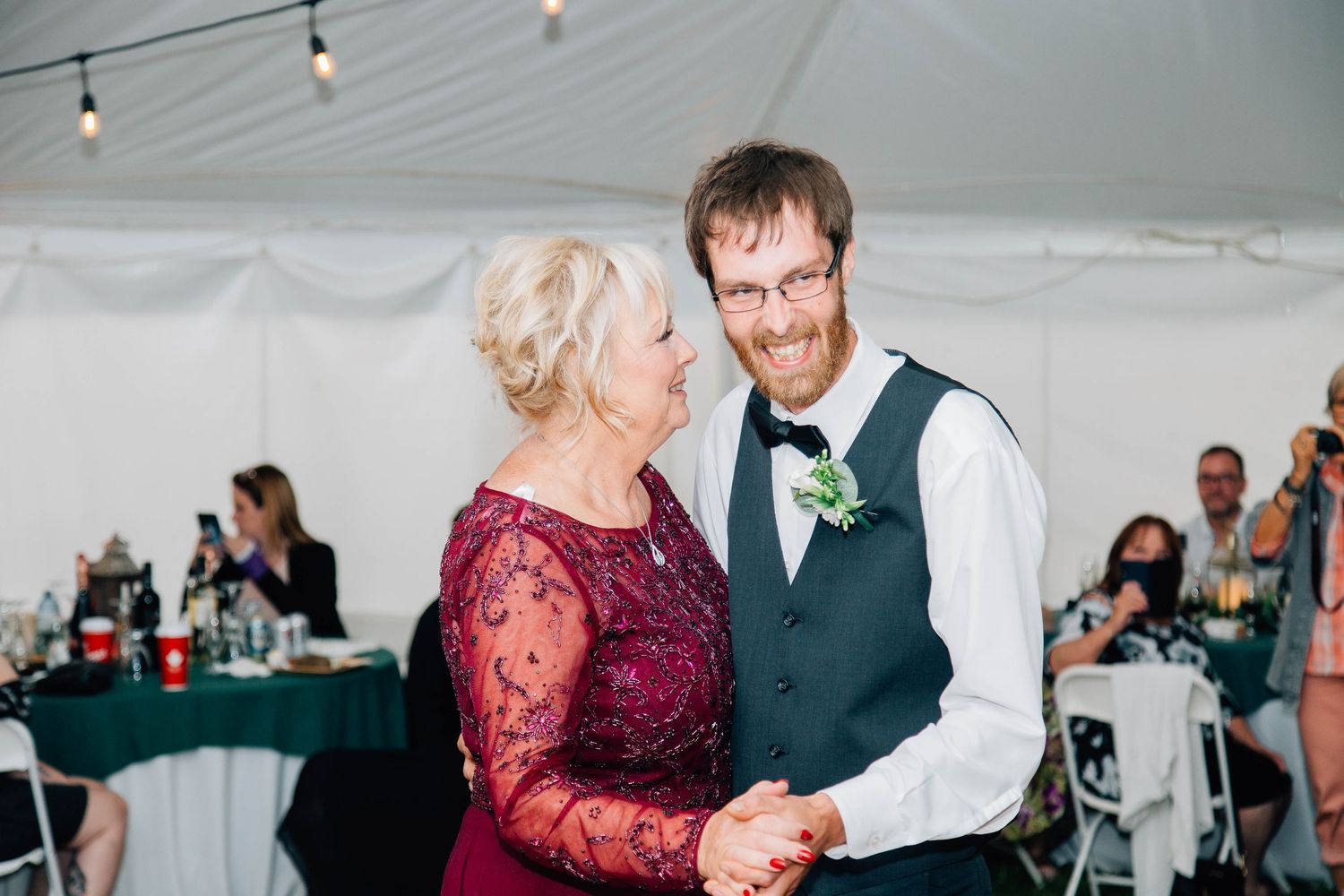 Groom shares emotional mother-son dance with mom in burgundy lace gown at wedding reception.