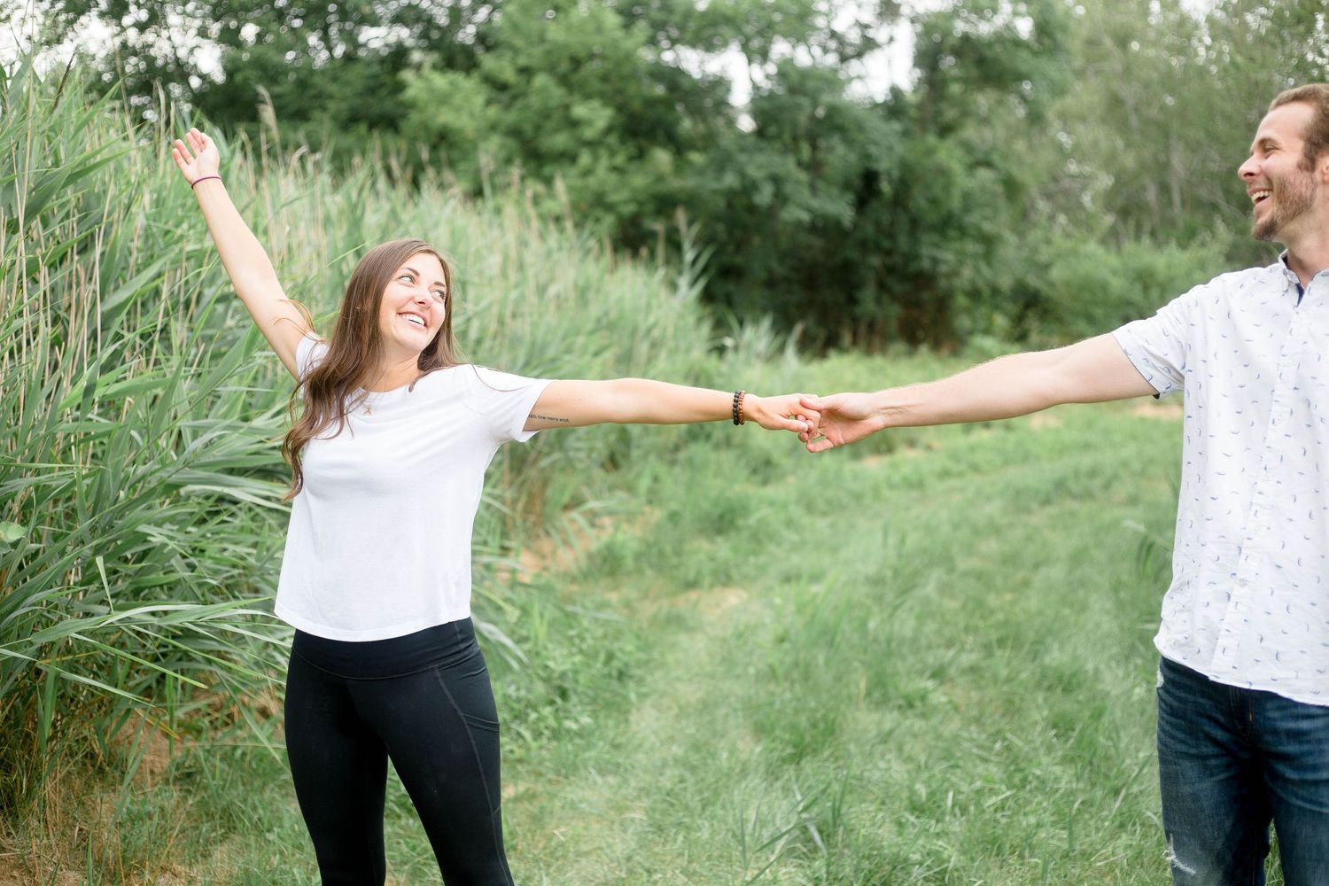 Woman raising her arm joyfully while holding hands with man in a field.