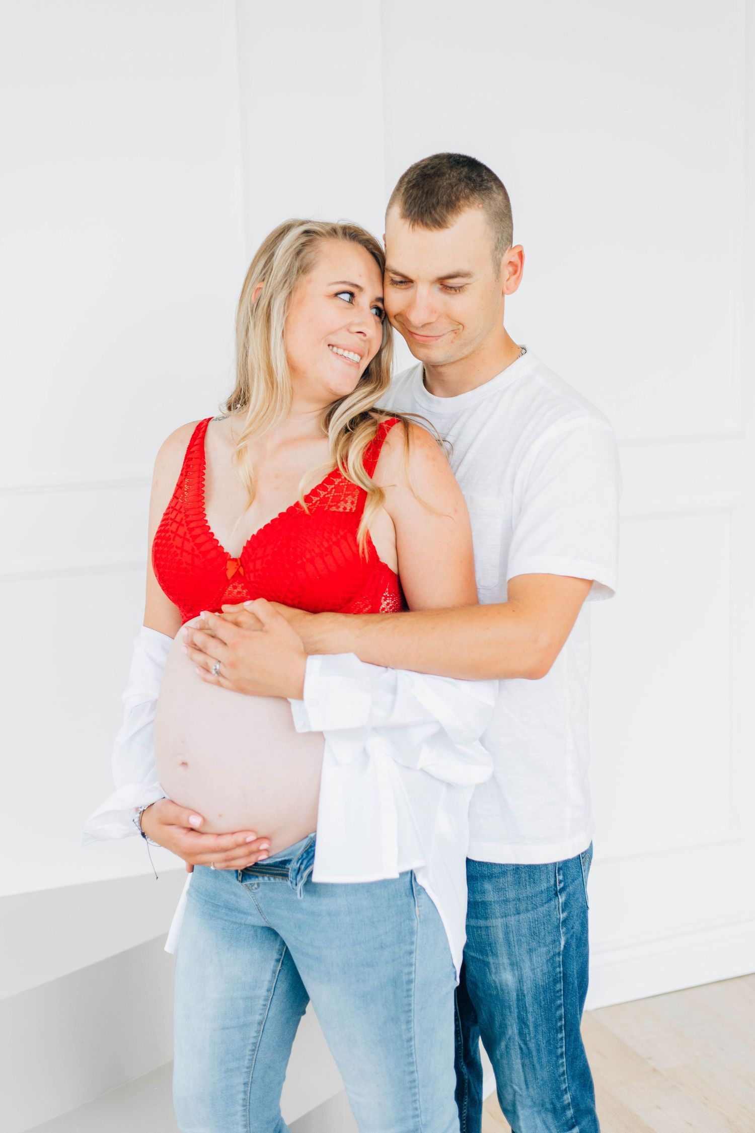 Couple embracing pregnant belly in white studio maternity photo.