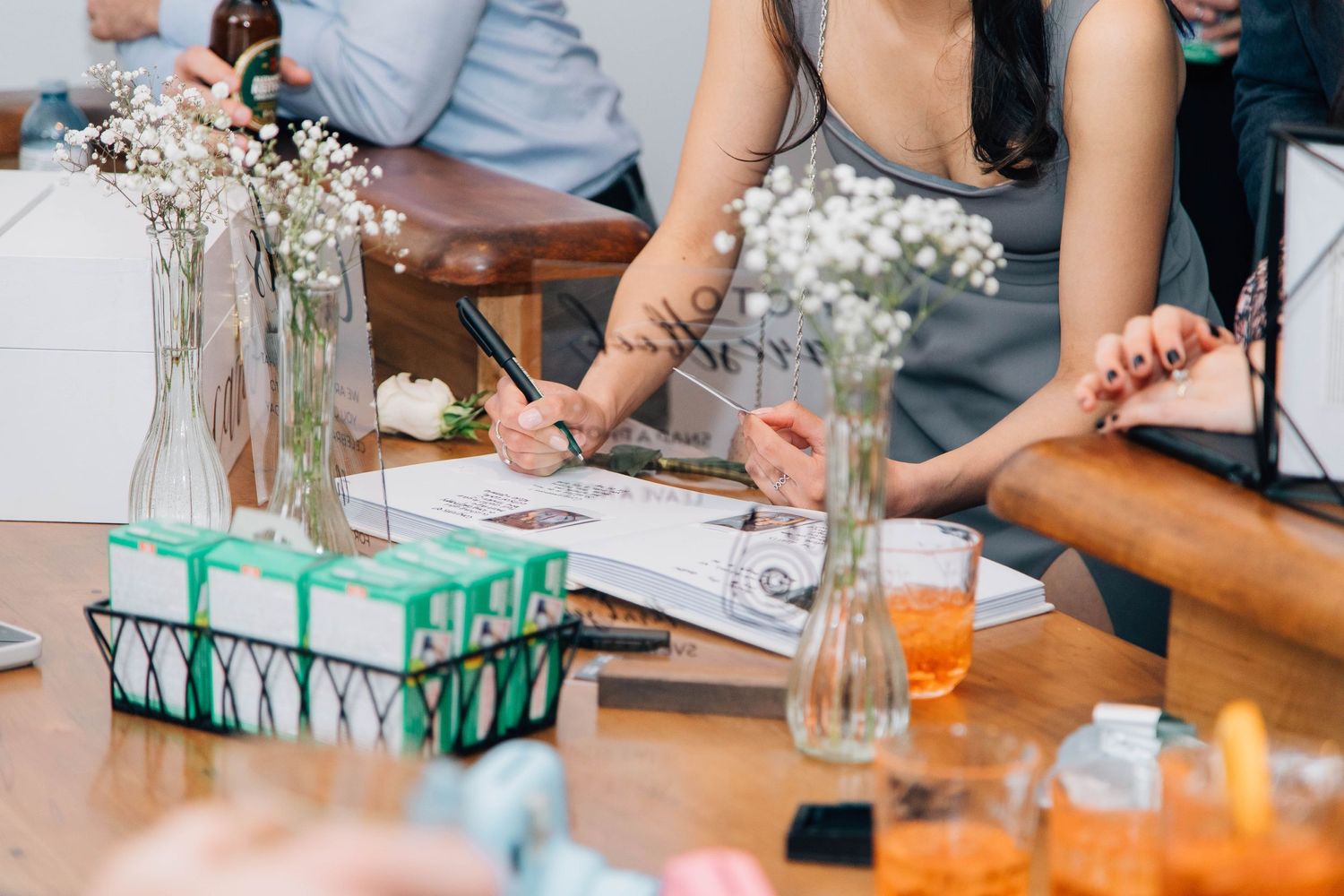 Wedding guest signing guestbook at decorated table with floral arrangements and gifts.