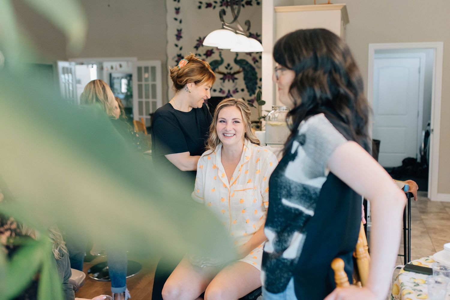 Smiling bride in floral pajamas chatting with bridesmaids during wedding morning preparations.