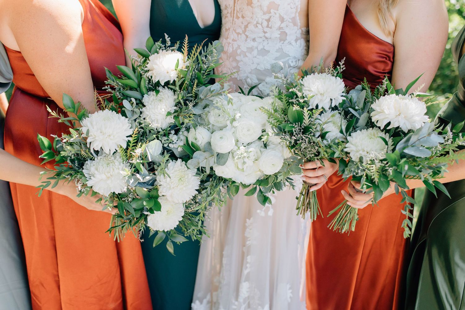 Close-up of wedding bouquets with white flowers and greenery held by bride and bridesmaids.