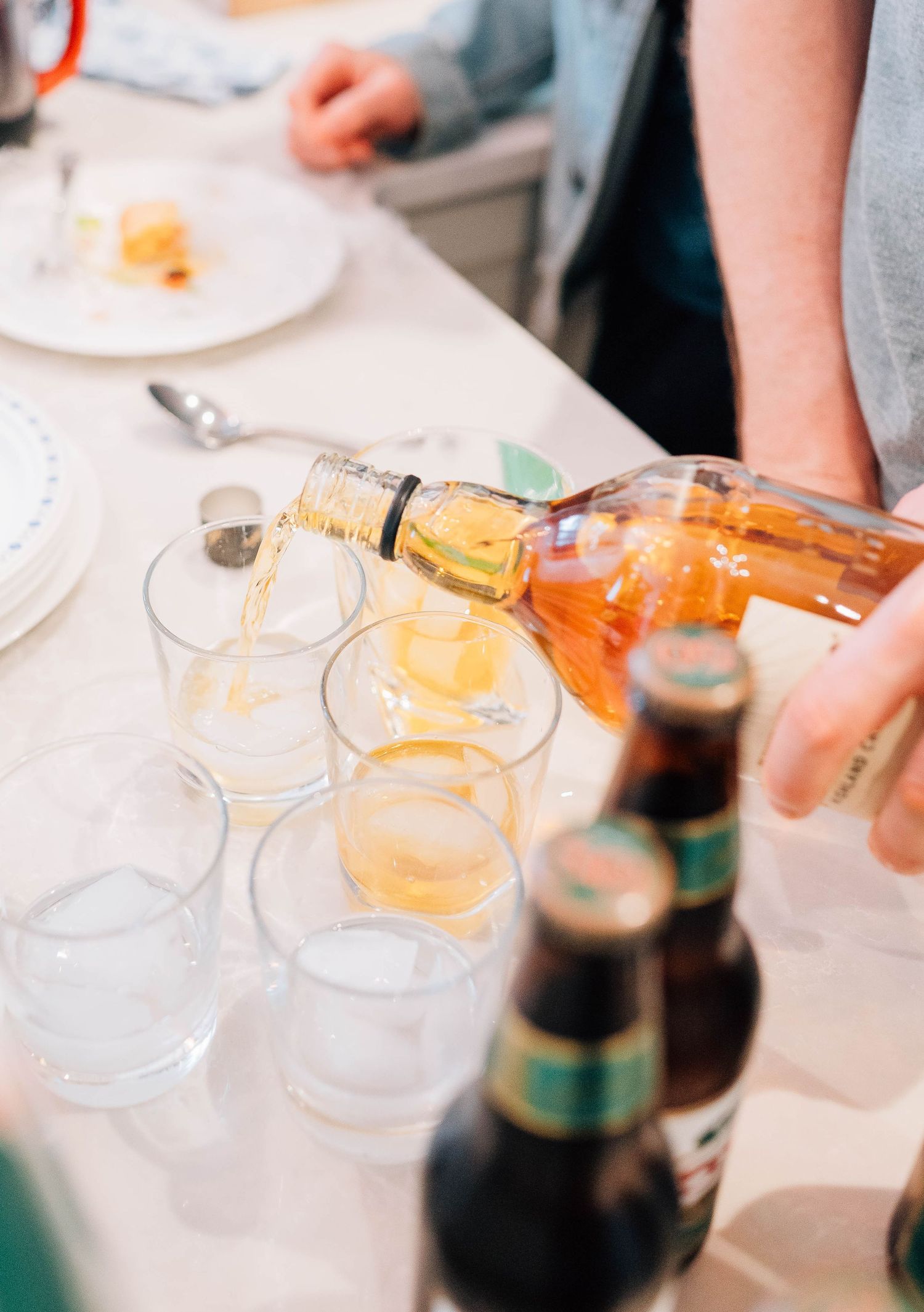Golden whiskey being poured into glasses beside beer bottles at a wedding reception celebration.