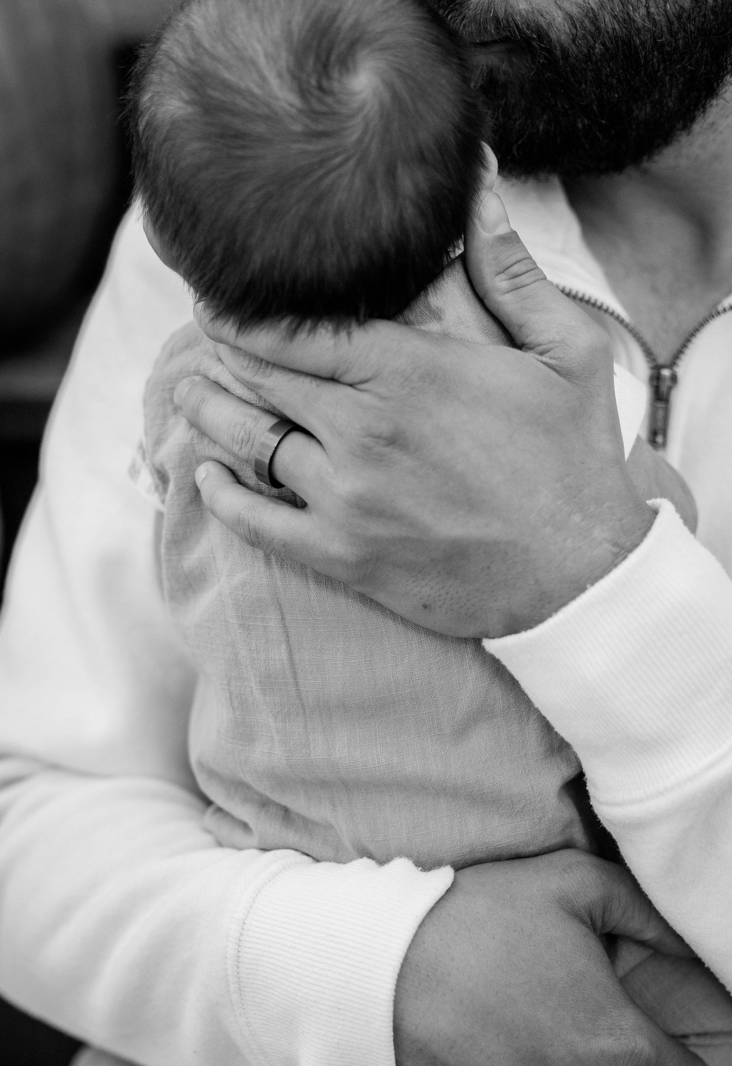 Black and white close-up of father cradling newborn baby wearing wedding ring.