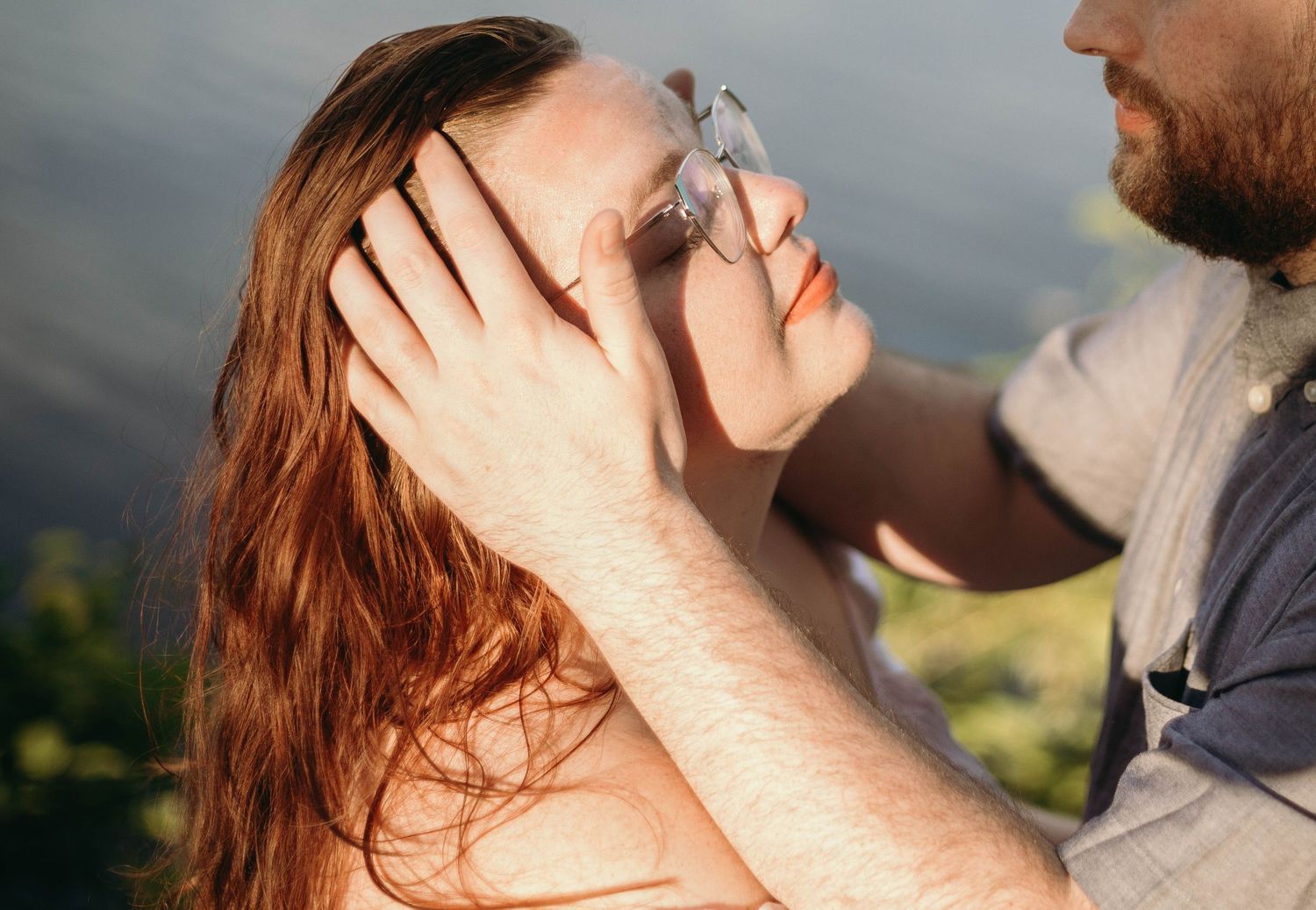 Man gently pushing hair from womans face outdoors with natural green bokeh background in warm light.