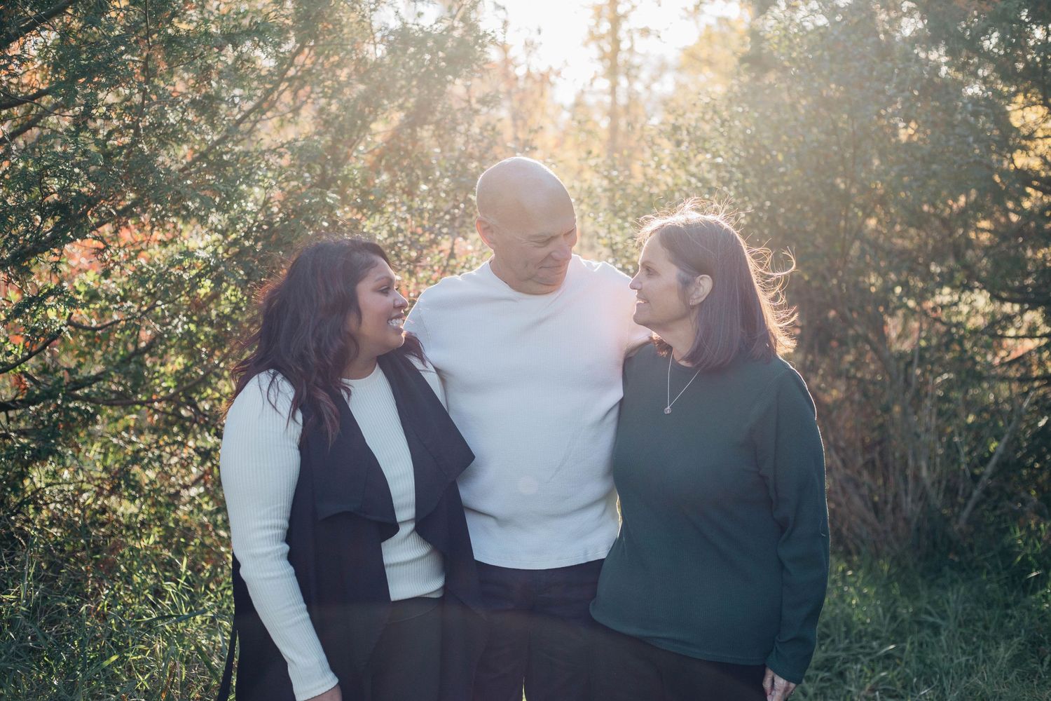 Three adults sharing a warm moment together laughing in a sunlit autumn forest setting.