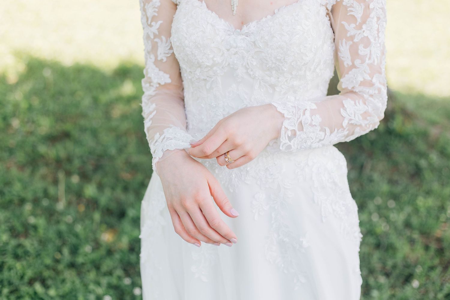 Close-up of bride in lace long-sleeve wedding gown with gold rings on her fingers.