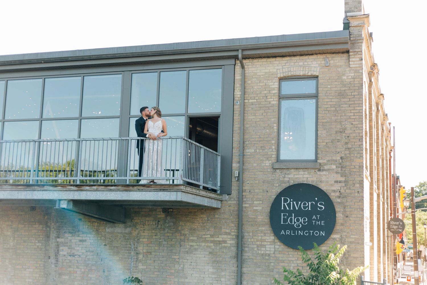 Bride and groom kissing on balcony of River's Edge Arlington venue at sunset.