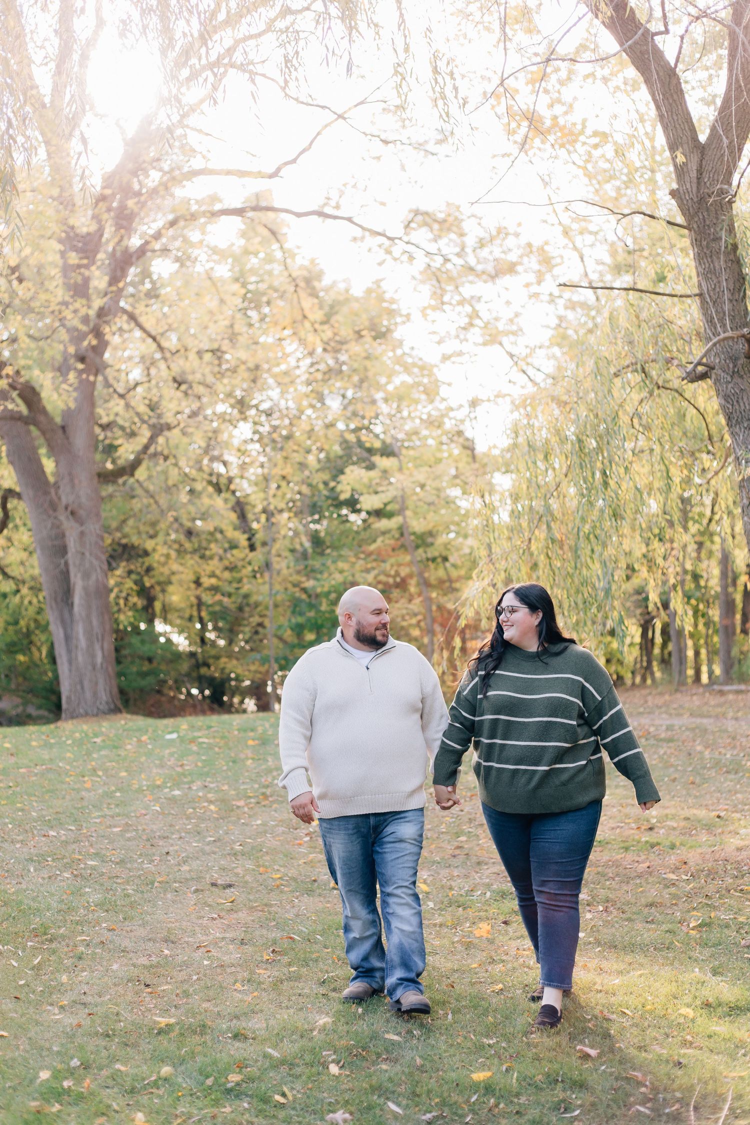 Couple holding hands walking through a sunny autumn park with colorful fall foliage.
