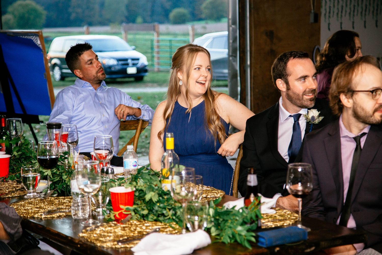 Wedding guests laughing and celebrating at decorated reception table with gold garland and greenery.