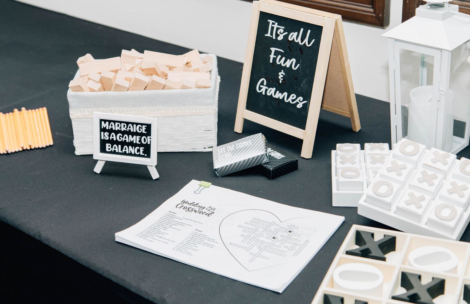 Wedding reception games table with Jenga, tic-tac-toe, and chalkboard signs reading Its all Fun and Games.