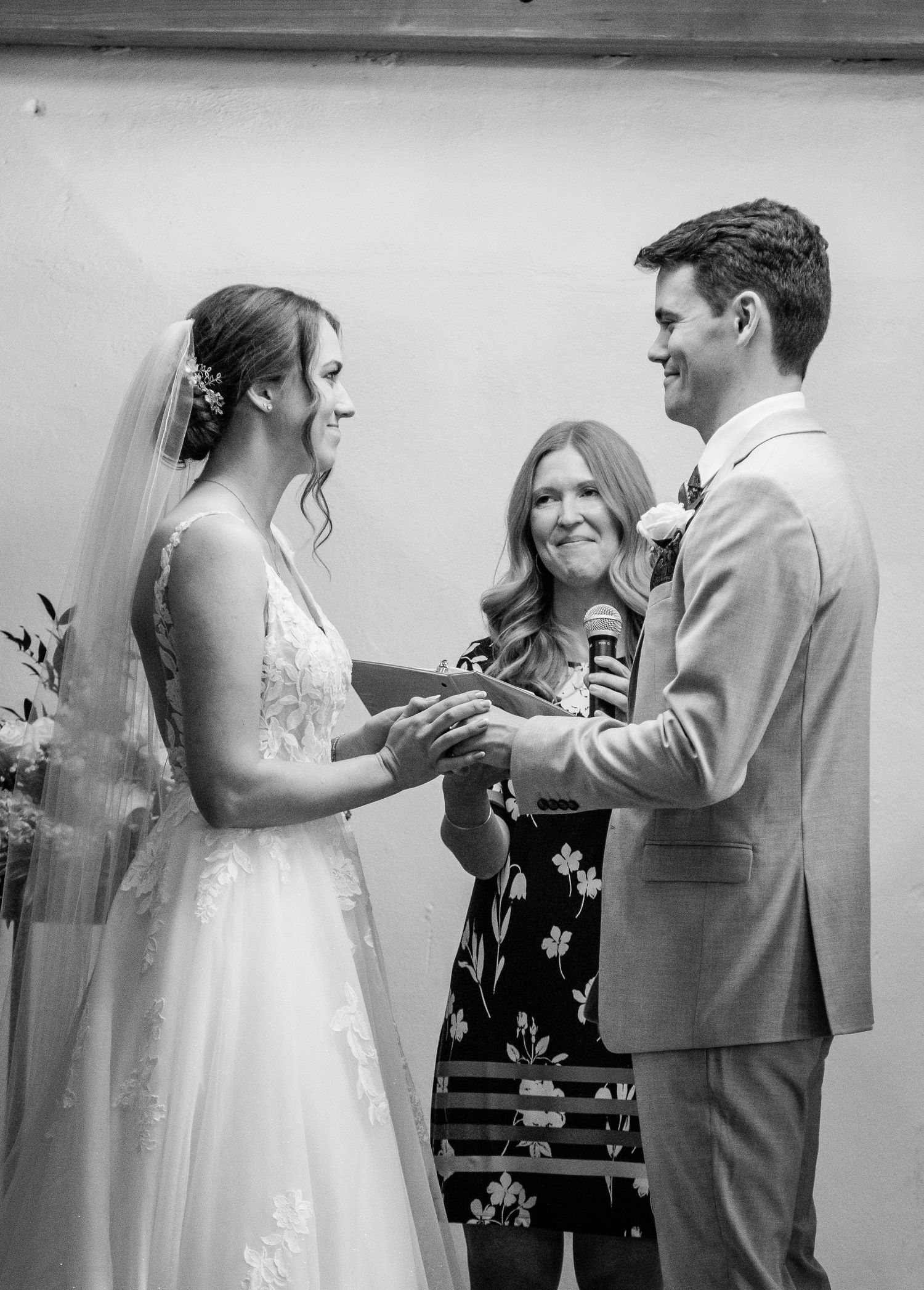 Black and white photo of bride placing ring on grooms finger during wedding ceremony.