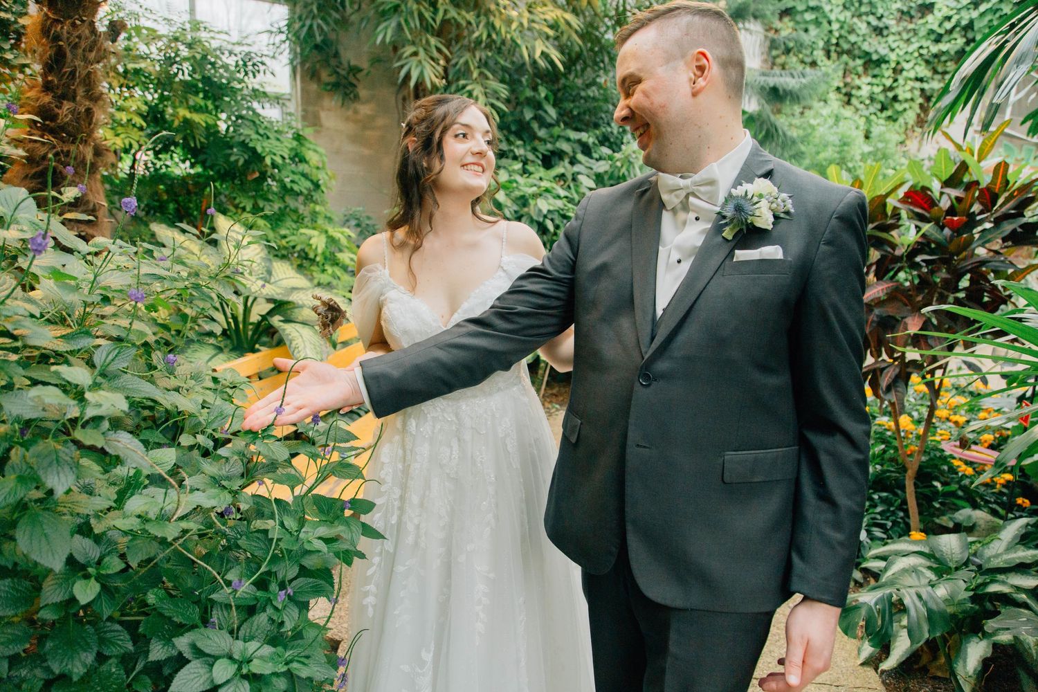 Bride and groom walking together among lush tropical greenery during wedding photo session.