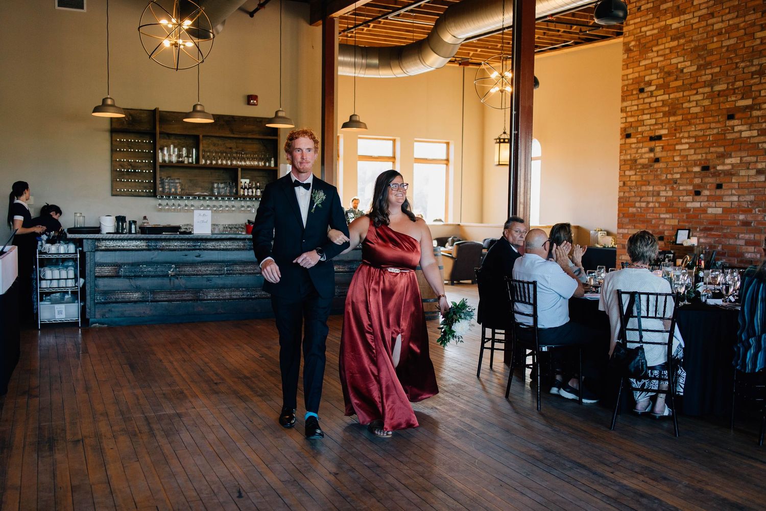 A couple in formal attire walks across a hardwood dance floor at an elegant wedding reception venue.