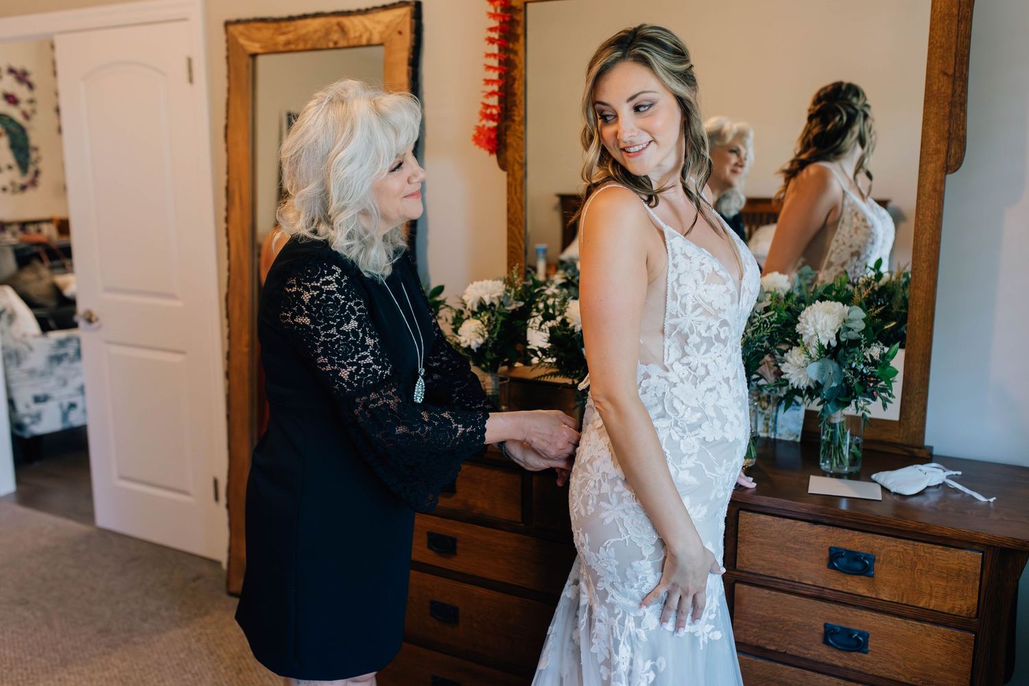 Mother helps bride fasten her lace wedding dress inside the family home before the ceremony.