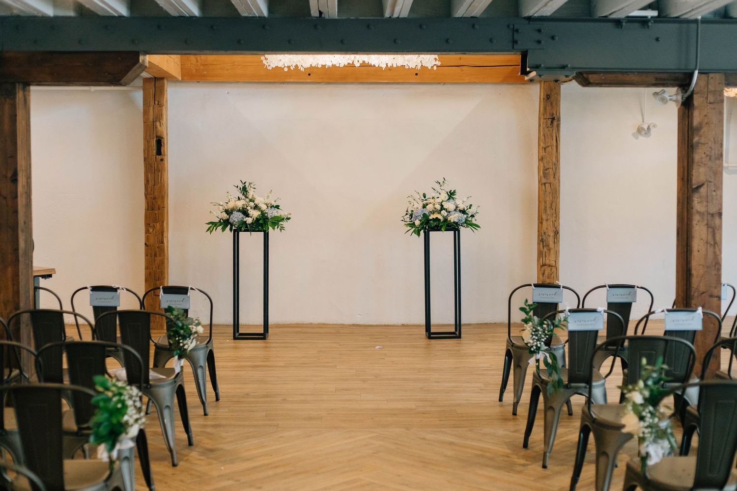 Elegant wedding ceremony venue with herringbone wood floors, black chairs, and floral arrangements.