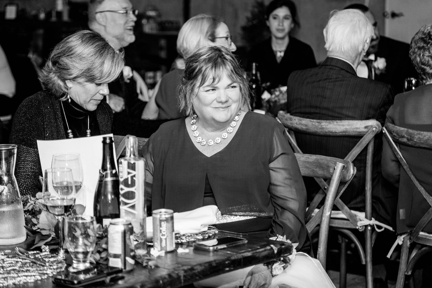 Black and white photo of elegantly dressed women smiling at festive wedding reception table.