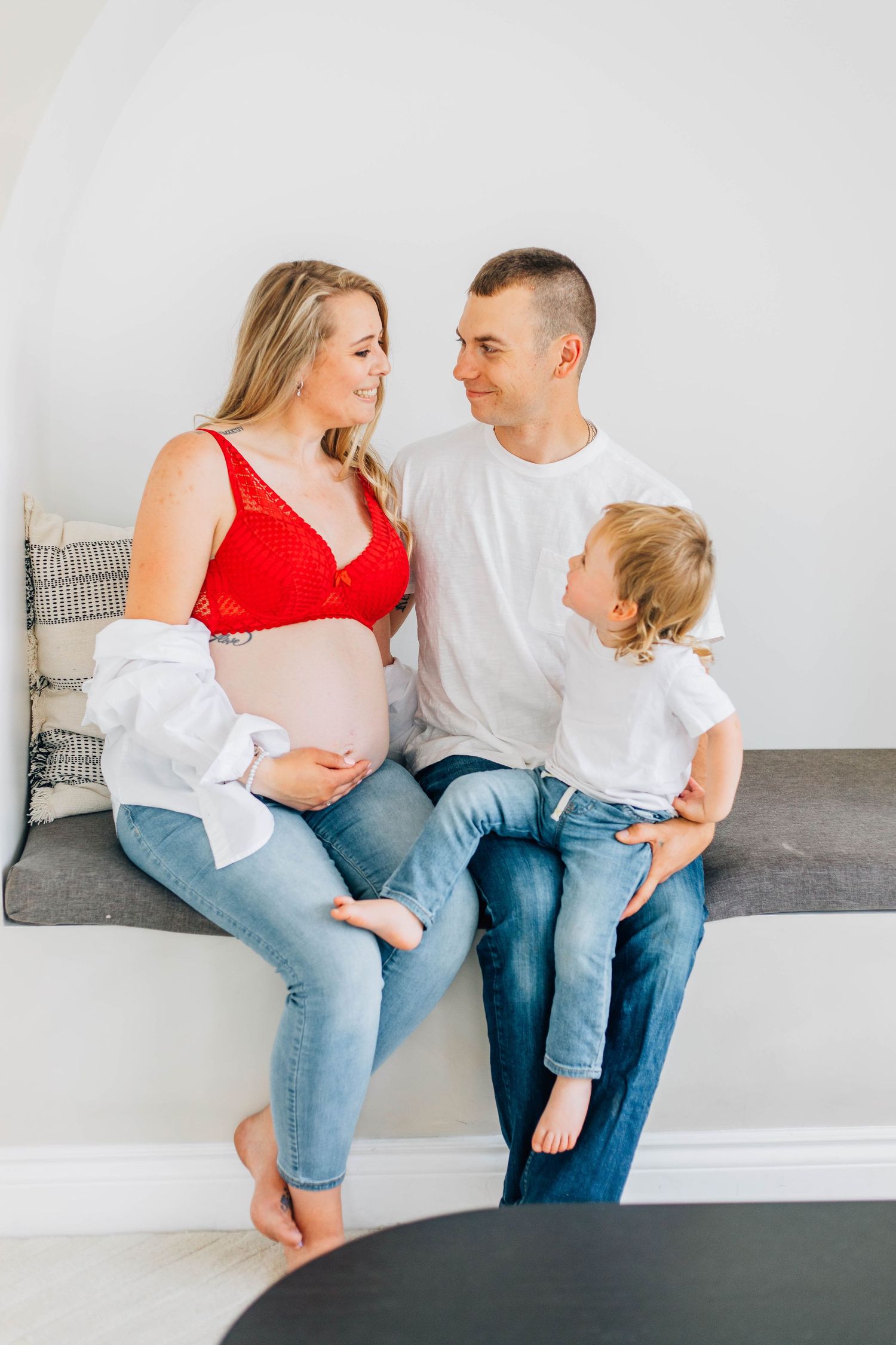 Loving family with pregnant mother, father, and young son sitting on bench looking at each other.