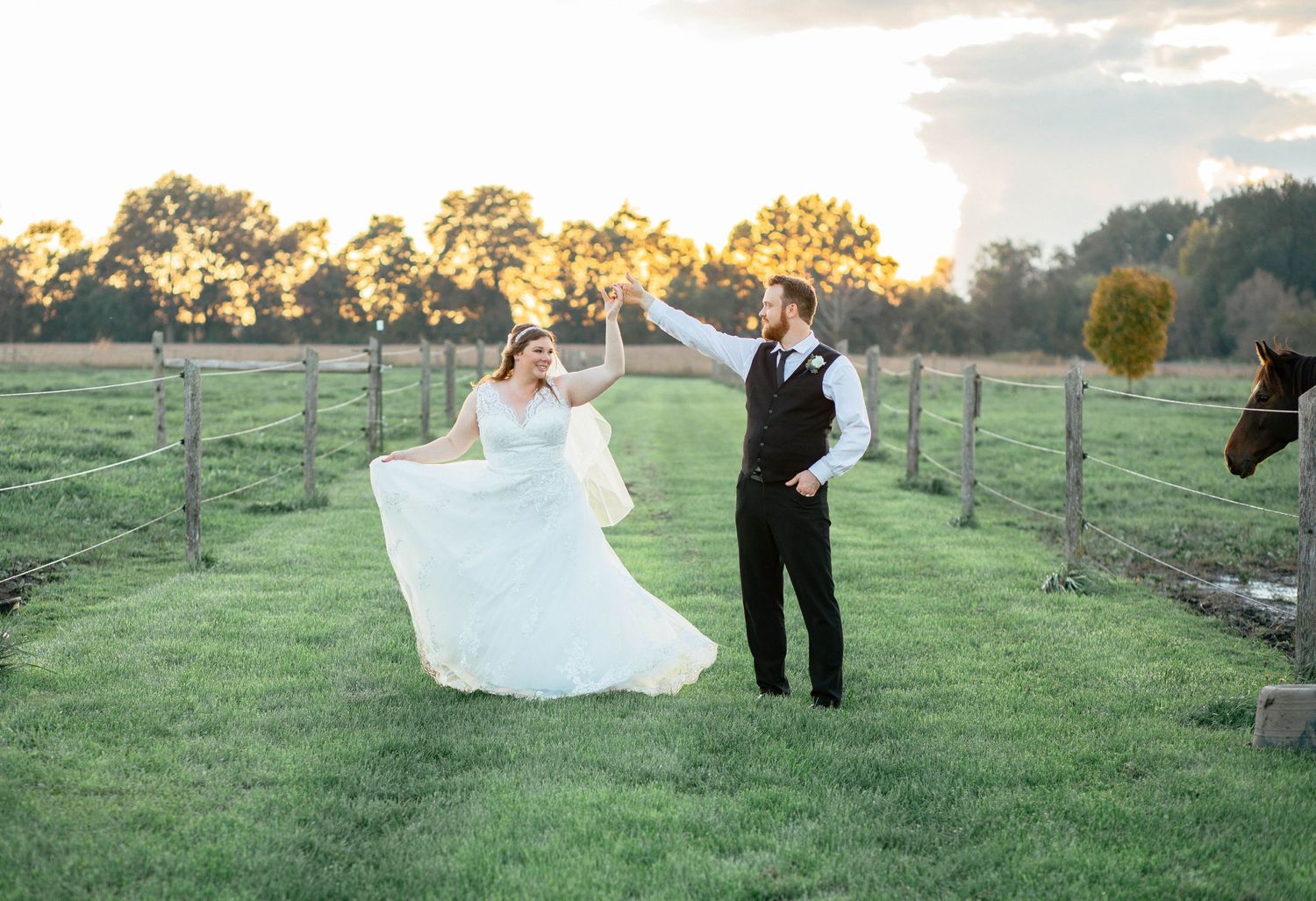 Groom spinning bride in a white gown on a sunny farm field at golden hour.