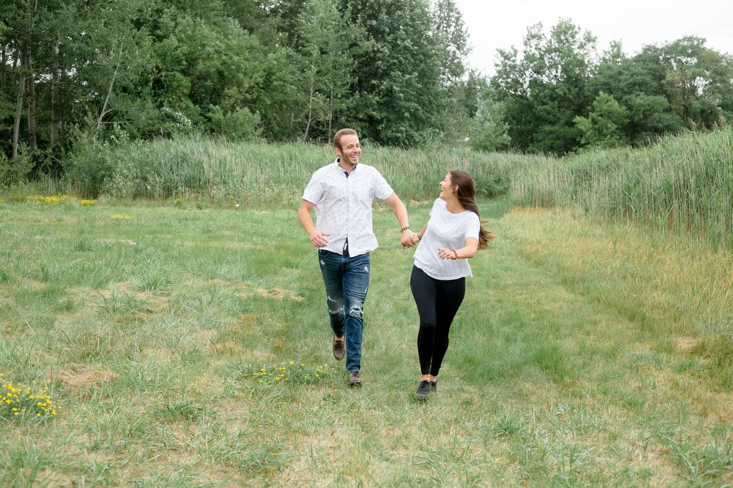 Happy couple holding hands running through a green meadow together.