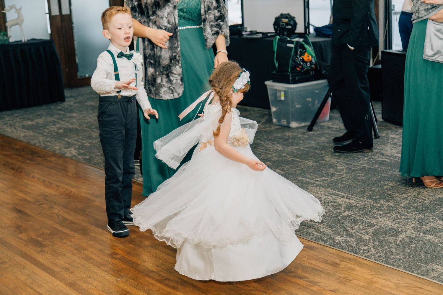 Joyful young boy in suspenders and flower girl dancing with wedding guests at reception celebration.
