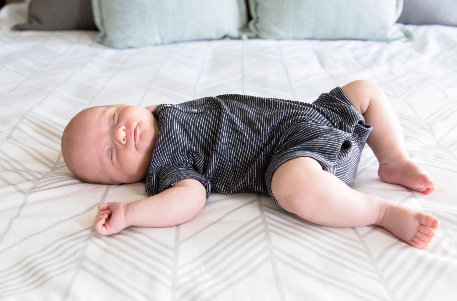 Peaceful newborn baby sleeping on a white patterned bed in striped onesie.