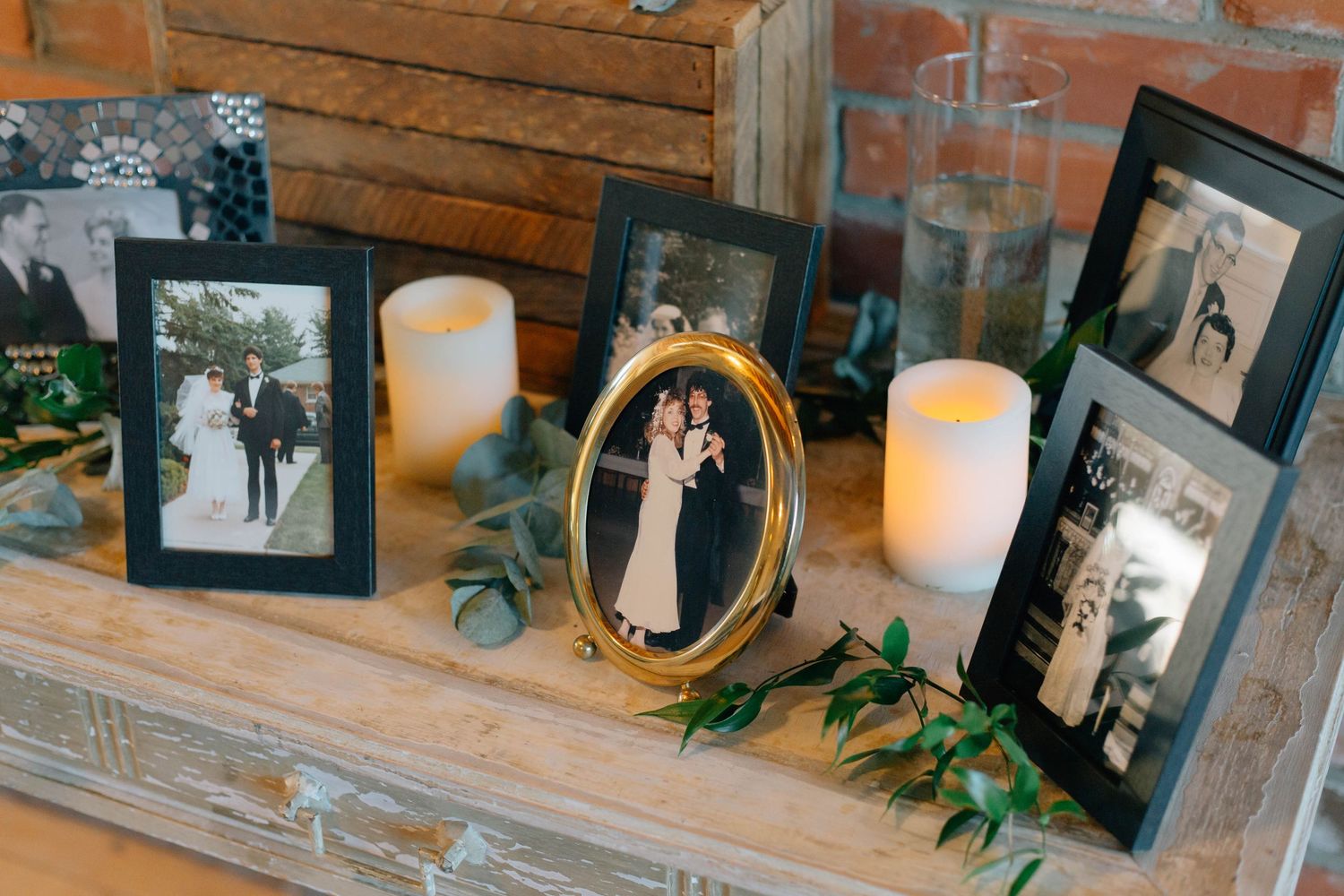 Framed vintage wedding photos and candles displayed on a rustic wooden mantle as wedding decor.