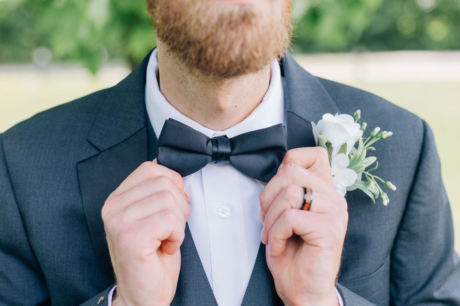 Groom adjusting his black bow tie wearing a navy suit with a white boutonniere.