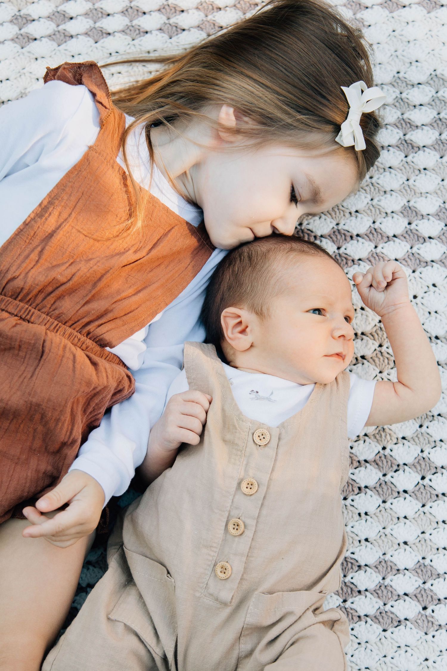 Young girl lying on blanket giving gentle kiss to newborn baby sibling.
