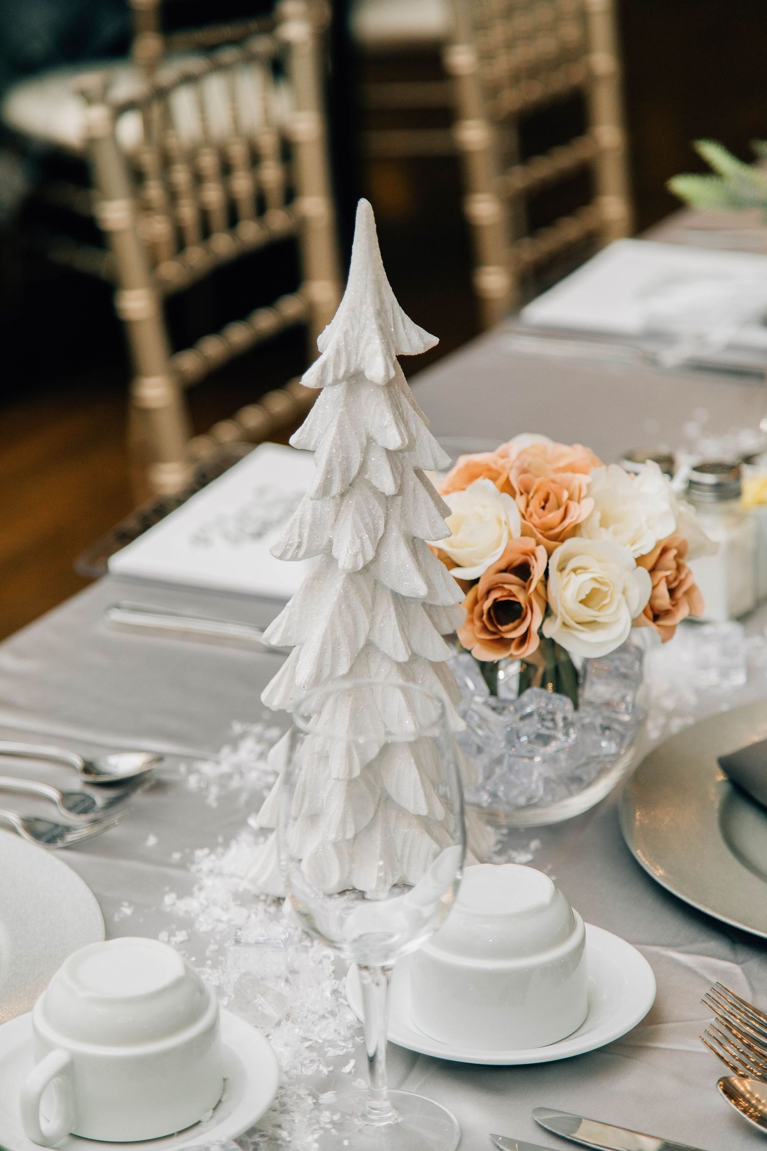 Winter wedding table centerpiece featuring a white ceramic Christmas tree and peach rose floral arrangement.