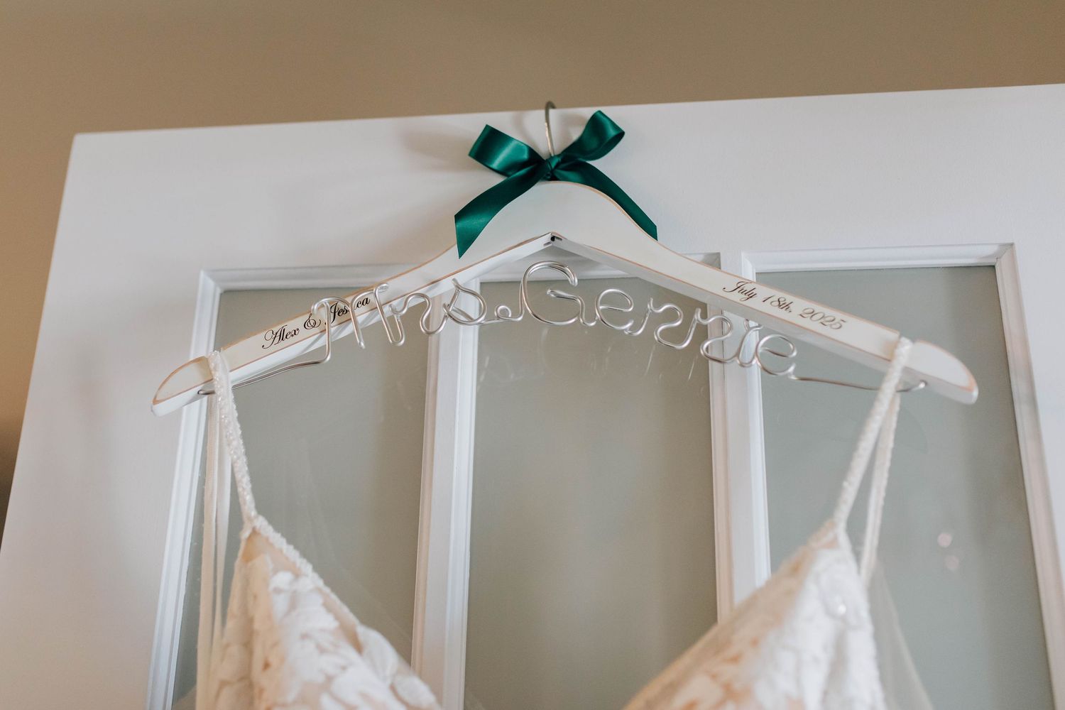Personalized white wire bridal hanger with green ribbon bow on glass door.