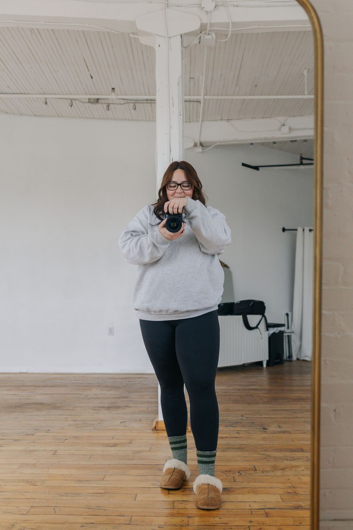 Photographer taking a mirror selfie in a bright white studio space holding a camera.