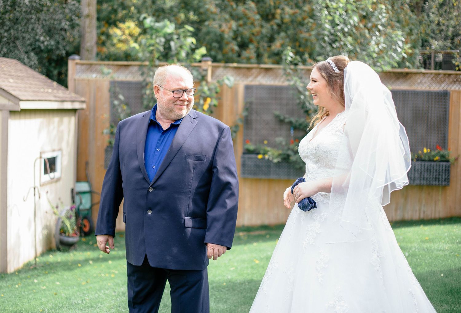 Father in navy suit sharing an emotional first look moment with his daughter in white wedding gown outdoors.