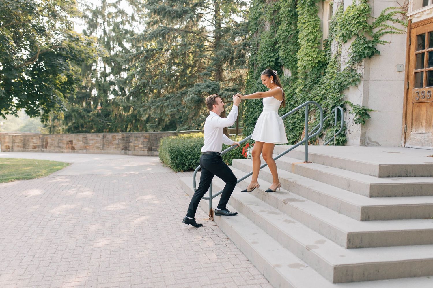 Couple dances playfully on stone steps outside ivy-covered building during engagement photo session.