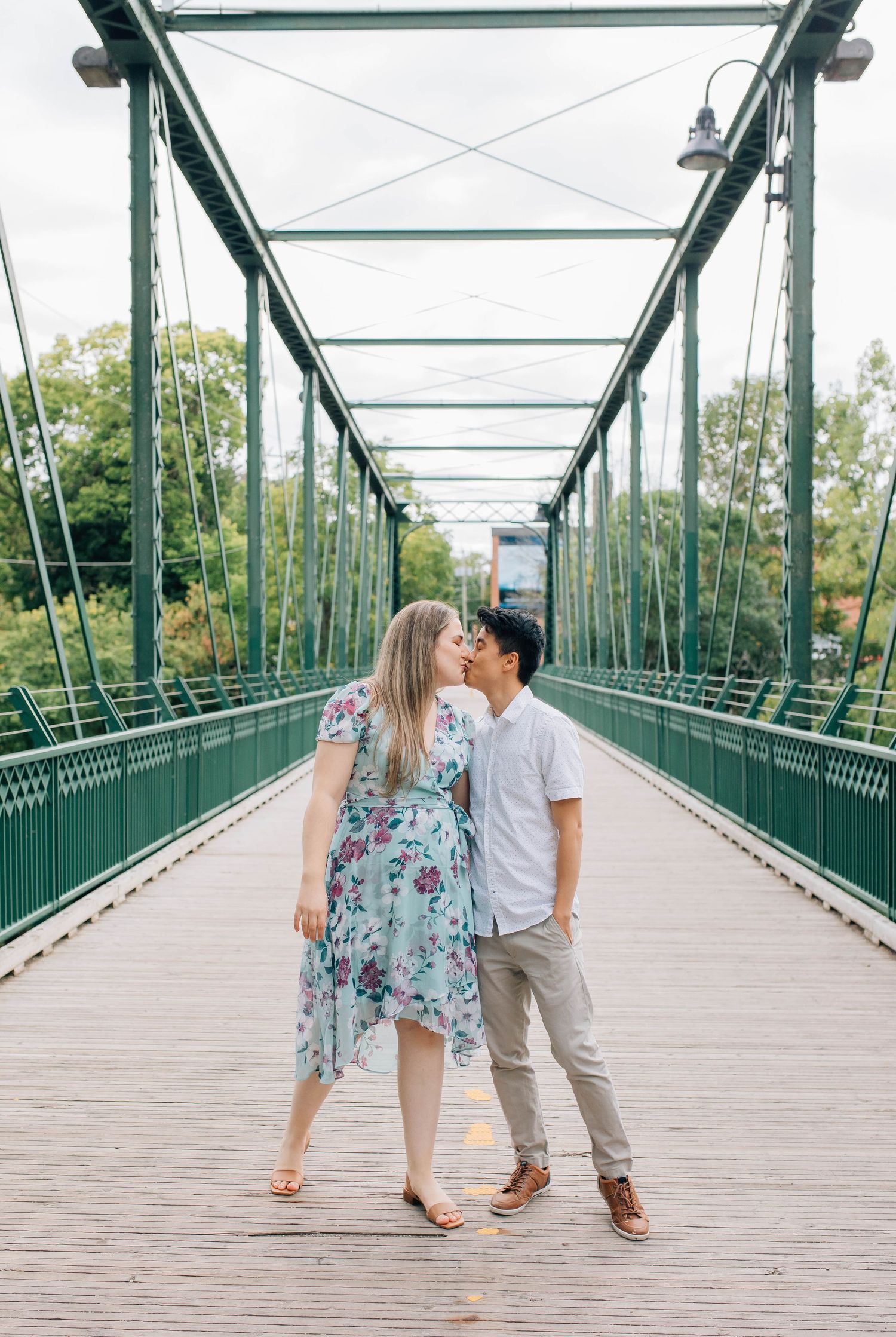 couple holding hands and kissing on a bridge in london ontario