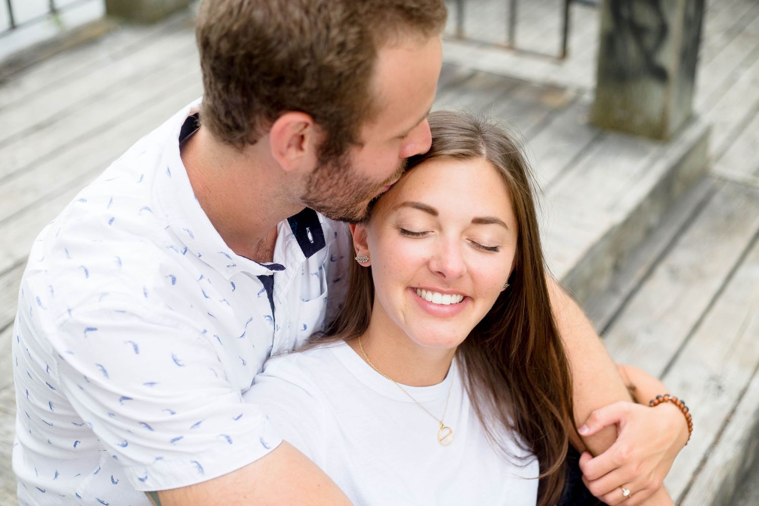 Man kissing woman on the head as she smiles with eyes closed outdoors.