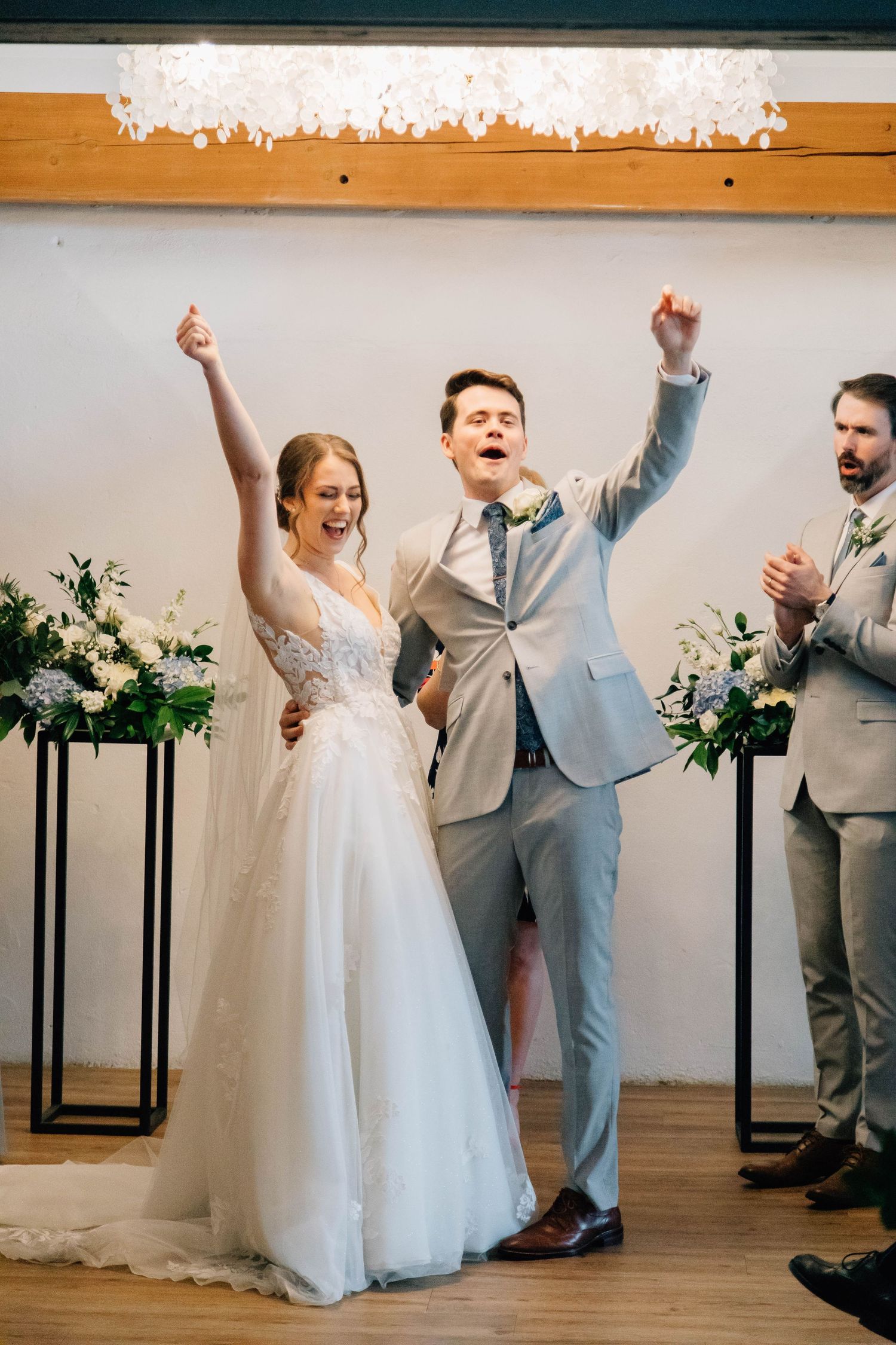 Excited newlyweds celebrating with raised arms after wedding ceremony with guests applauding.
