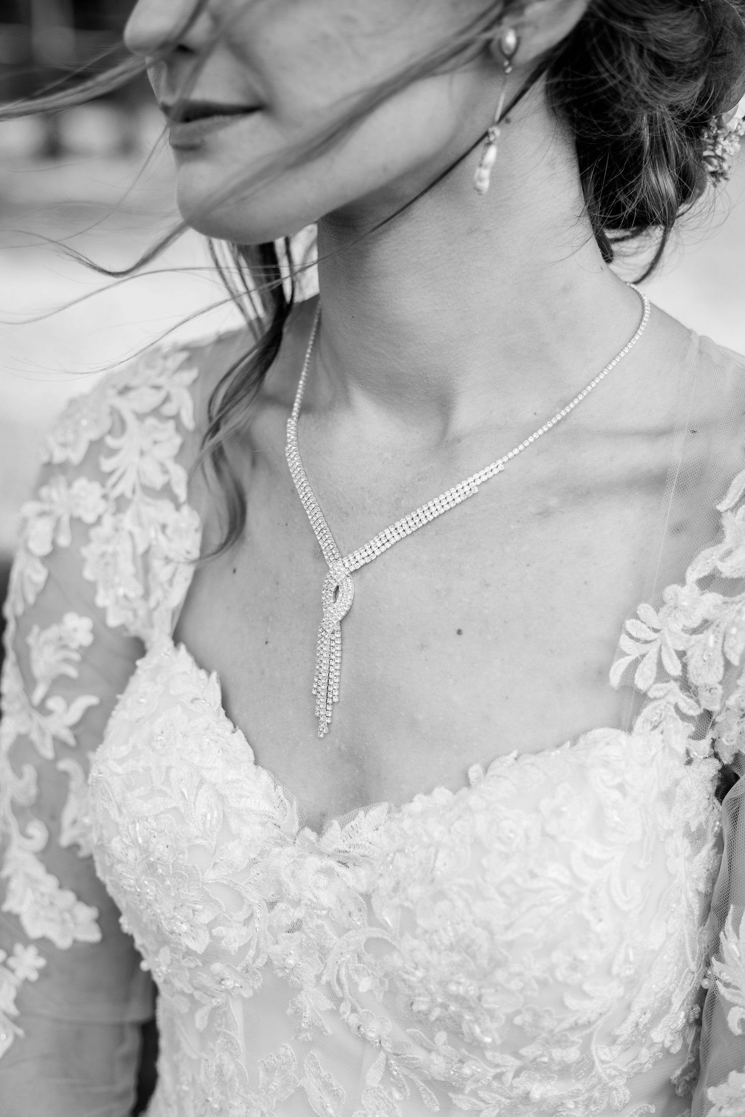 Black and white close-up of a bride wearing a lace wedding dress and elegant diamond drop necklace.