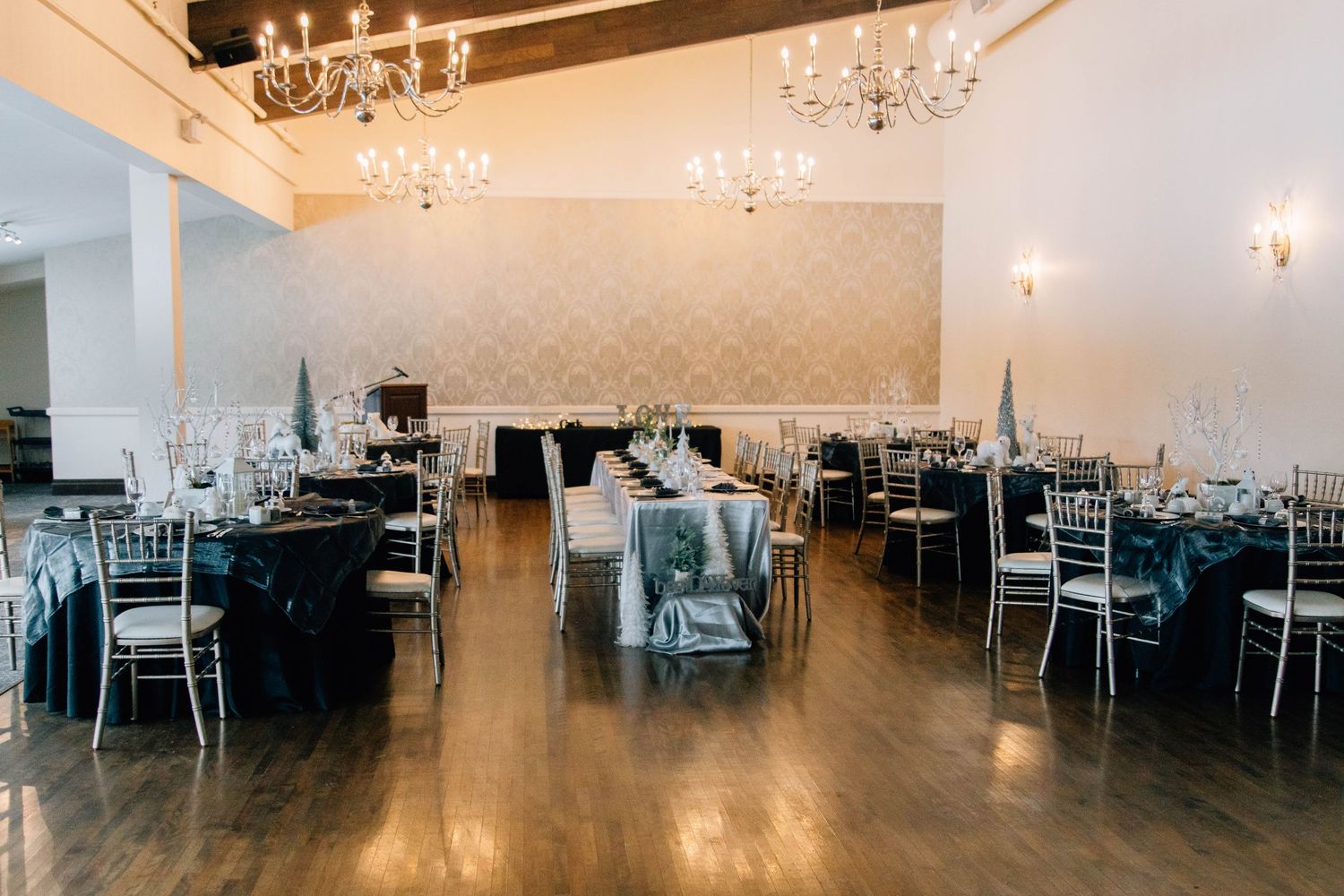 Elegant winter wedding reception hall with navy blue tablecloths, white branch centerpieces, chiavari chairs, and crystal chandeliers.
