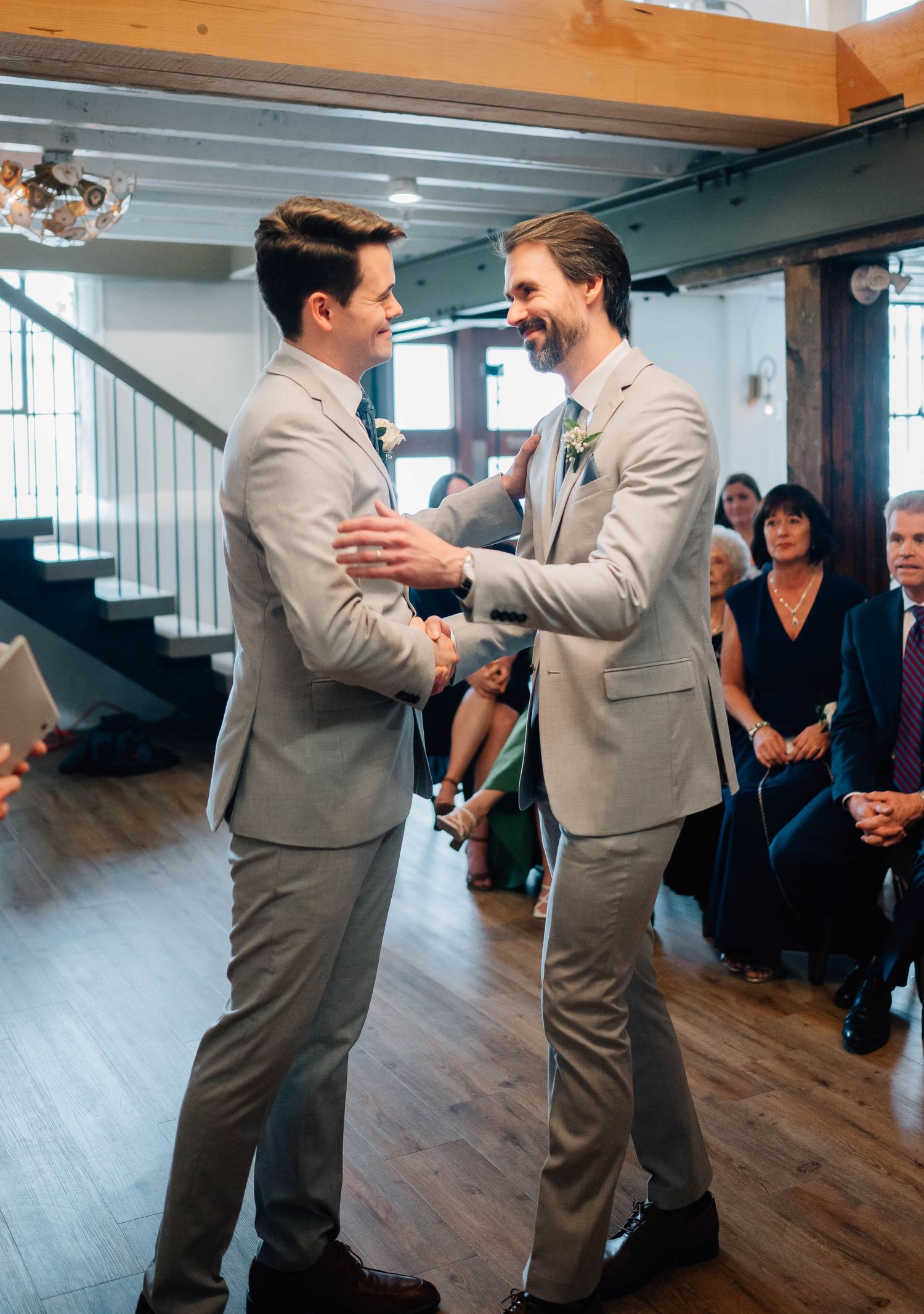 Two groomsmen in matching grey suits sharing a joyful moment at wedding.
