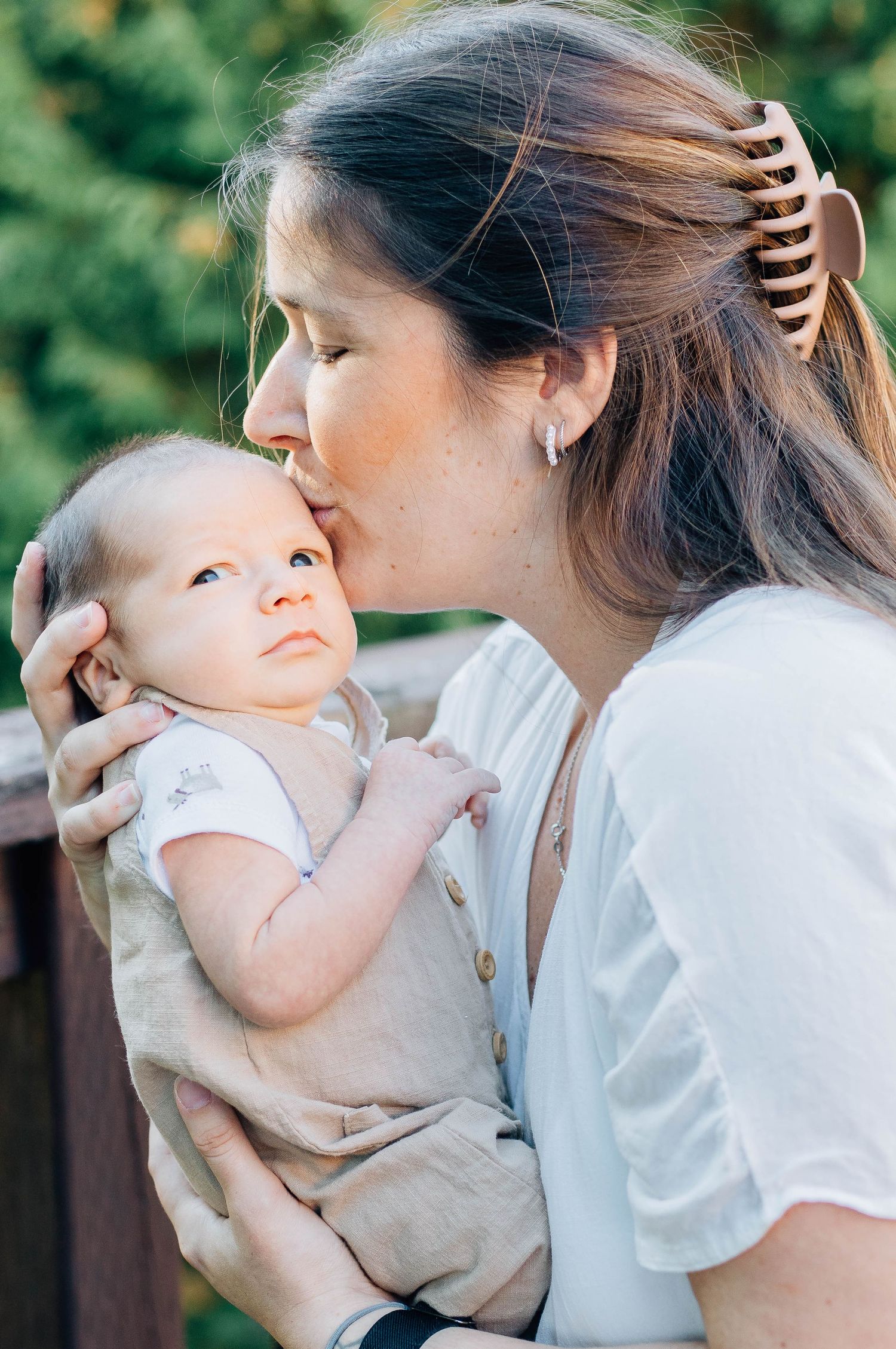 Loving mother kissing newborn baby on cheek while holding infant outdoors.